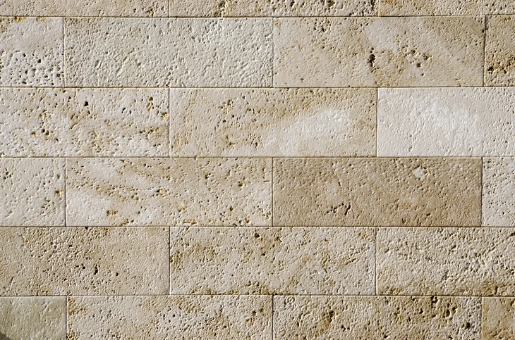 Mur intérieur revêtu de carrelage en pierre naturelle beige à texture poreuse, disposé en format rectangulaire avec joints fins