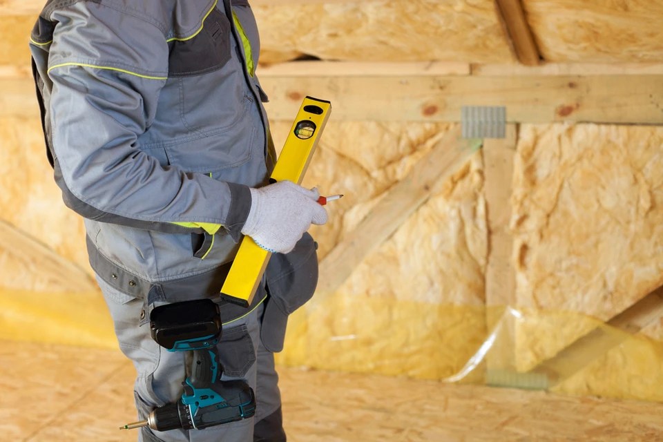 Ouvrier en tenue de travail grise avec liserés jaunes utilisant un niveau à bulle jaune sur chantier de construction intérieur