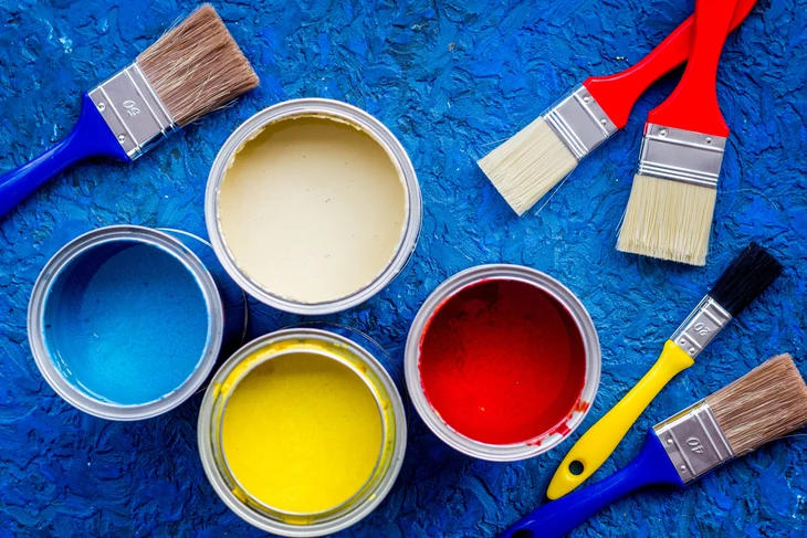 Scène d'atelier de peinture avec pots de peinture ouverts aux couleurs vives - bleu, jaune, rouge et beige - disposés sur surface texturée bleue