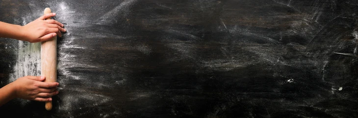 Scène d'atelier avec mains tenant un rouleau à pâtisserie en bois sur surface de travail noire enfarinée