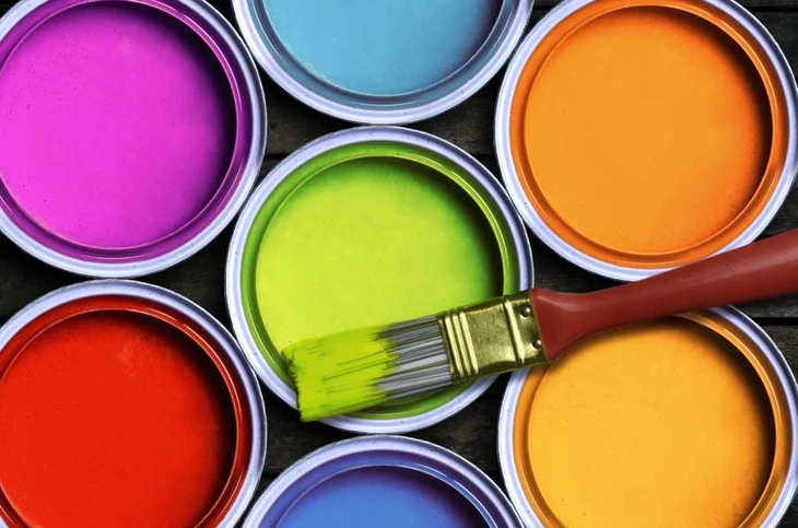 Pots de peinture ouverts aux couleurs vives disposés sur surface sombre avec pinceau plat à manche bois trempé dans peinture vert lime