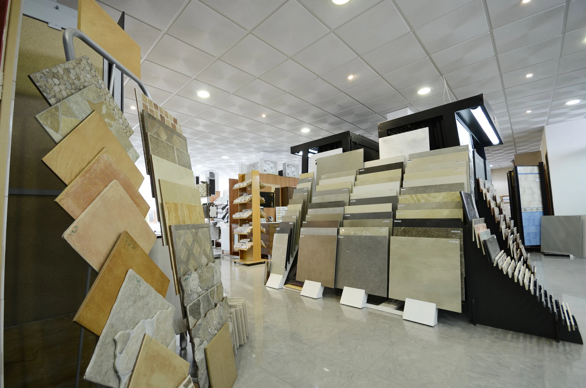 Showroom intérieur de revêtements avec présentoirs muraux et au sol exposant diverses gammes de carrelages, pierres naturelles et matériaux de construction