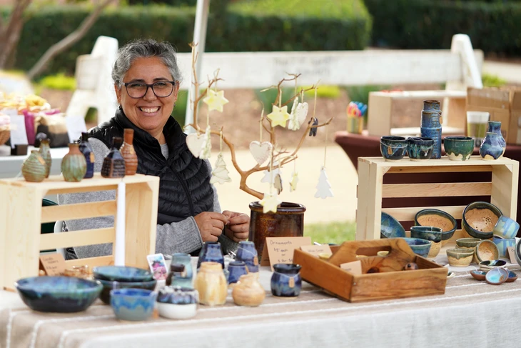 Une artisan potière souriante présente ses créations céramiques sur un marché artisanal en plein air