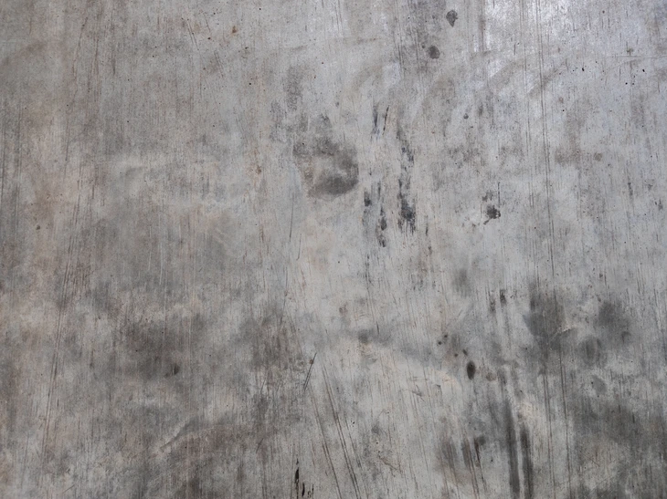 Surface en béton brut d'aspect industriel présentant des traces d'usure et de vieillissement naturel dans un environnement intérieur ou extérieur urbain