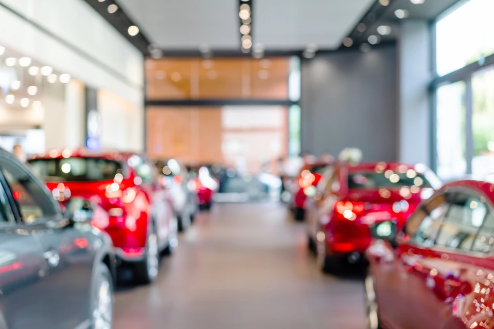 Showroom automobile moderne avec véhicules exposés, majoritairement rouges et gris, disposés sur un sol carrelage clair