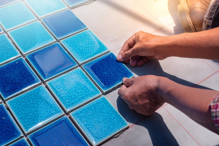 Artisan posant des carreaux de mosaïque bleus sur une surface extérieure ensoleillée