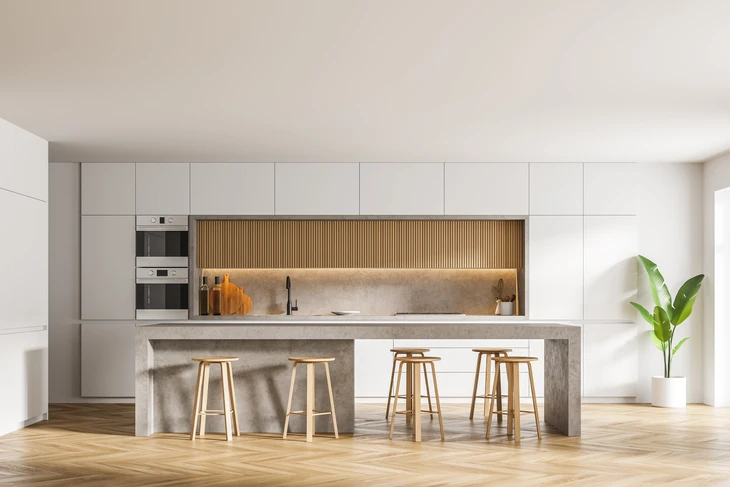 Cuisine moderne ouverte avec îlot central en béton, four et micro-ondes encastrés, tabourets en bois naturel