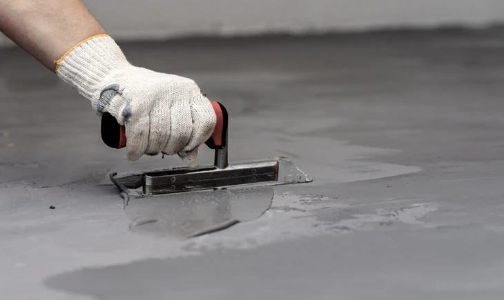Ouvrier effectuant des travaux de finition sur dalle de béton en extérieur, utilisant une taloche métallique pour lisser la surface