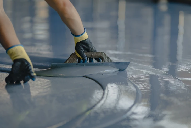 Travailleur appliquant un enduit de lissage sur une surface en béton à l'aide d'une taloche métallique