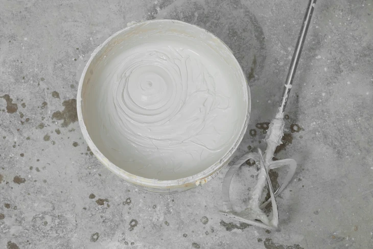 Atelier de peinture intérieur avec seau de peinture blanche au sol, mélangeur électrique professionnel immergé