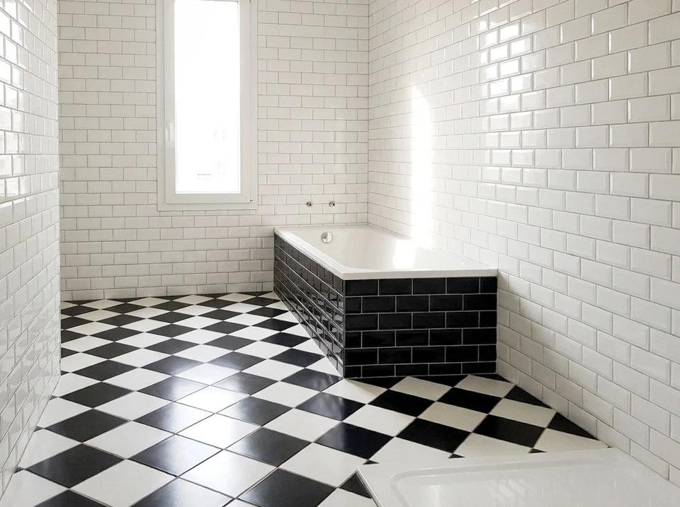 Photographie d'un intérieur résidentiel moderne avec un sol en carrelage élégant (couleur neutre ou intemporelle) posé au sein d'un espace de vie convivial. La pièce doit montrer le carrelage en contexte d'utilisation réelle (cuisine ou salle de bains par exemple), avec un aménagement soigné et du mobilier contemporain. L'éclairage doit être naturel ou chaleureux, mettant en valeur la texture et la qualité du revêtement posé. L'image doit transmettre un sentiment d'intemporalité, de confort et de raffinement.